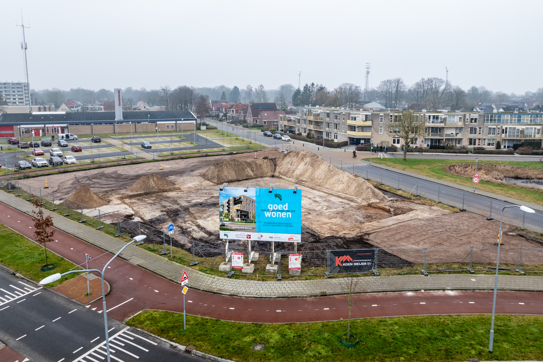 Afgegraven gebied Acantus nieuwbouwwoningen met een groot blauw bord met de tekst Goed wonen, met elkaar maken we het en de tekst 32 middenhuurappartementen aan de Sorghvlietlaan in Veendam.